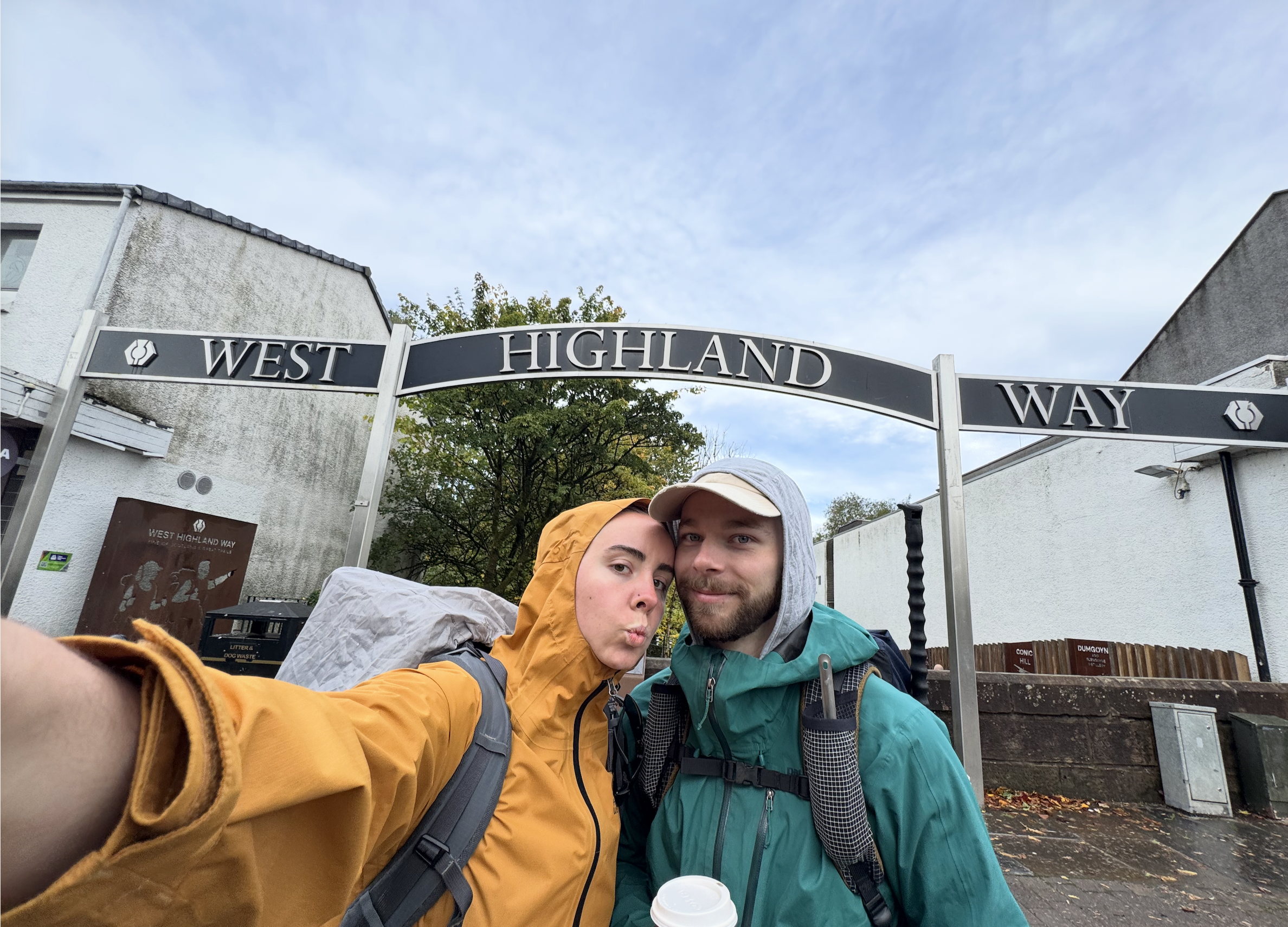 Two hikers in rain shells under the West Highland Way arch.